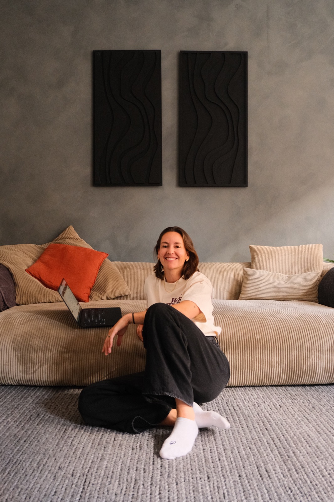 Fiona Raikes sitting on the floor of her living room with her laptop, smiling at the camera